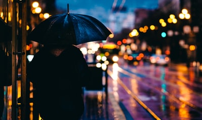 人走在大街上,手里拿着黑伞在夜间汽车在公路边
